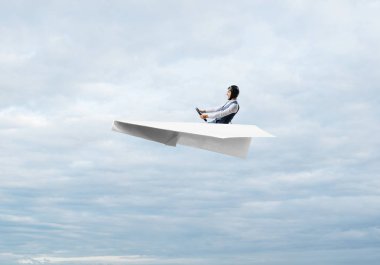 Havacı şapkalı işadamı kağıt düzlemde oturuyor ve direksiyonu tutuyor. Bulutlu mavi gökyüzünde kağıt uçak kullanan pilot. Ekstrem havacılık hobisi. Kabarık bulutlu gökyüzü panoraması.