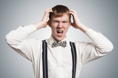 Stresli hippi öfkeyle bağırıyor ve ellerini başının üstünde tutuyor. Duygusal kızıl oğlanın yüzünde tahriş olmuş bir ifade var. Adamın portresi gri arka planda beyaz gömlek, papyon ve pantolon askısı takıyor.