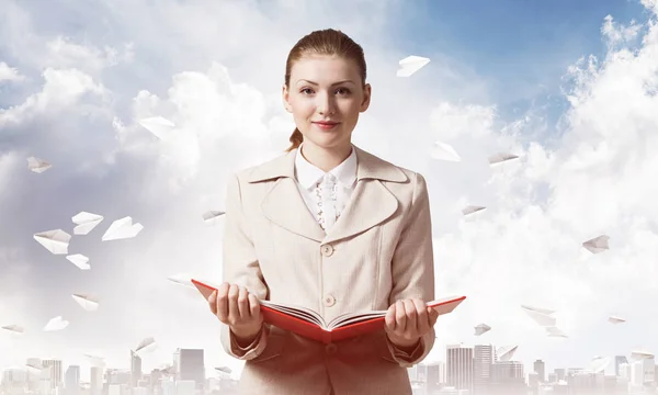 迷人的女人拿着打开的笔记本背景的城市景观和纸飞机在蓝天 优雅的年轻女子穿着白色西装 手里拿着打开的书 在公司实习与实习 — 图库照片