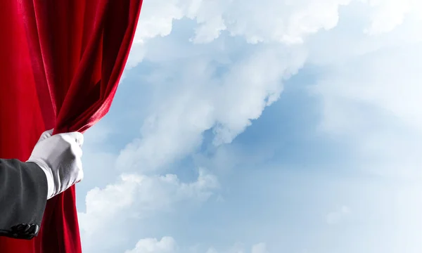 Paisaje nublado detrás de la cortina roja y la mano sosteniéndolo — Foto de Stock