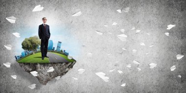 Yeşil yüzen adada beton zemine karşı duran kendine güvenen zarif iş adamı.