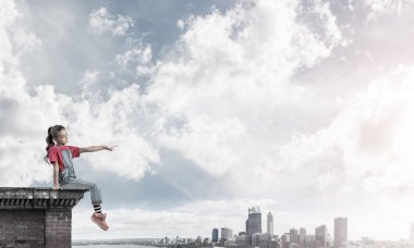 Üstte oturan ve bir şeyi işaret eden sevimli bir kız.