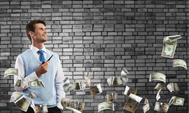 Kendinden emin ve genç işadamı akıllı-casual giyim yasaktır boru duran dolar uçan arasında ve arka plan üzerinde gri karanlık duvara yatay çekim.