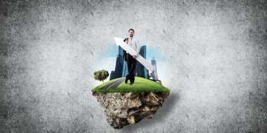 Takım elbiseli genç ve kendine güvenen bir iş adamının uçan adada gri beton arka planda dururken elinde büyük beyaz bir ok tutmasının kavramsal görüntüsü.