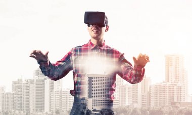 Sanal gerçeklik kulaklığı olan genç bir adam ya da şehrin arka planında 3 boyutlu gözlüklü.