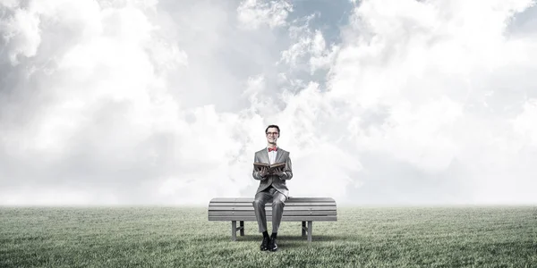 一个戴着红色眼镜 穿着西服 坐在长椅上看书的有趣男人 — 图库照片
