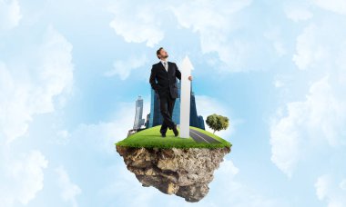 Kendinden emin ve başarılı işadamı siyah elbiseli Adası ve bulutlu gökyüzü arka plan üzerinde uçan üzerinde dururken onun elinde büyük beyaz ok ile ters işaret.