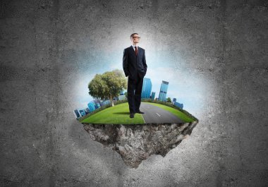 Yeşil yüzen adada beton zemine karşı duran kendine güvenen zarif iş adamı.