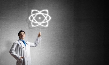 Başarılı ve beyaz üniformalı genç bir doktor, arka planda gri beton duvara karşı dururken moleküler yapıyla etkileşime giriyor..