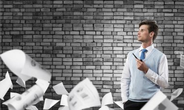 Kendinden emin ve genç işadamı akıllı-casual giyim yasaktır boru duran kağıtları uçan arasında ve arka plan üzerinde gri karanlık duvara yatay çekim.