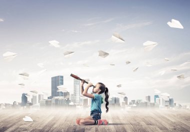 Ahşap zemin ve etrafında uçan kağıt uçaklar üzerinde oturan sevimli kız