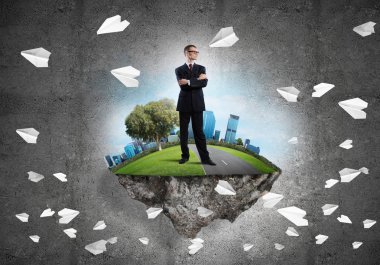 Yeşil yüzen adada beton zemine karşı duran kendine güvenen zarif iş adamı.