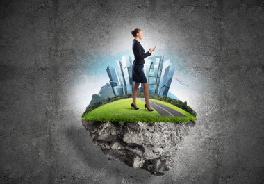 Yeşil yüzen adada beton zemine karşı duran kendine güvenen zarif bir iş kadını.