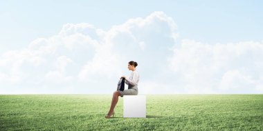 Elinde bavuluyla beyaz küpün üzerinde oturan zarif bir iş kadını.