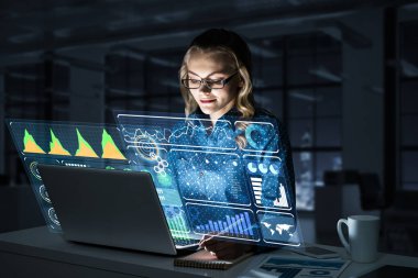 Çekici bir kadın gece ofisinde oturmuş dizüstü bilgisayarına bakıyor. Karışık ortam