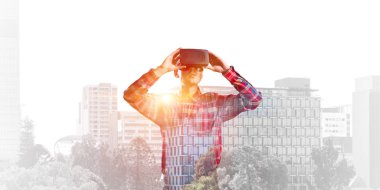 Sanal gerçeklik kulaklığı olan genç bir adam ya da şehrin arka planında 3 boyutlu gözlüklü.