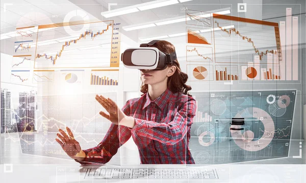 Educational process with help of VR headset. Cheerful young woman in checkered shirt using digital media interface while sitting indoors of office building.