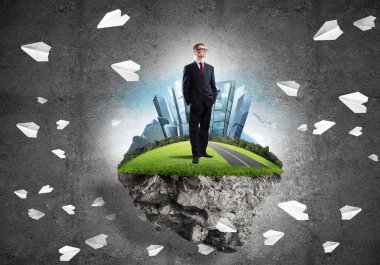 Yeşil yüzen adada beton zemine karşı duran kendine güvenen zarif iş adamı.