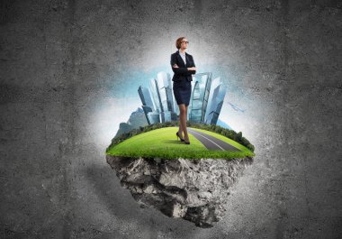 Yeşil yüzen adada beton zemine karşı duran kendine güvenen zarif bir iş kadını.