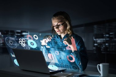 Çekici bir kadın gece ofisinde oturmuş dizüstü bilgisayarına bakıyor. Karışık ortam