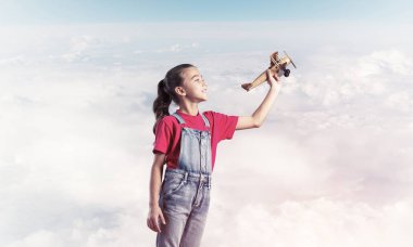 Elinde retro uçak modeliyle tulumlu şirin bir kız çocuğu.