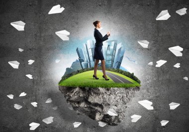 Yeşil yüzen adada beton zemine karşı duran kendine güvenen zarif bir iş kadını.