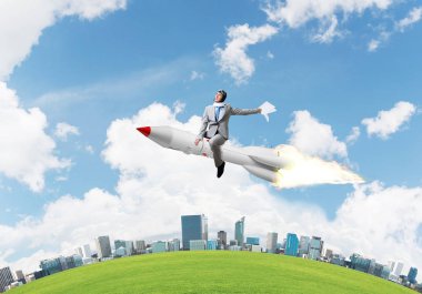 Cityscape ve mavi gökyüzü arka plan üzerinde ile roket üzerinde uçan takım elbiseli genç işadamı kavramsal görüntü.