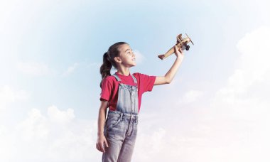 Elinde retro uçak modeliyle tulumlu şirin bir kız çocuğu.