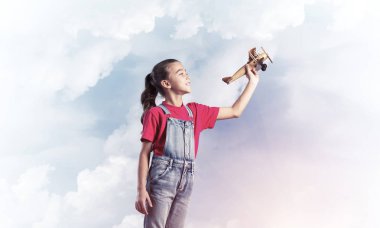 Elinde retro uçak modeliyle tulumlu şirin bir kız çocuğu.