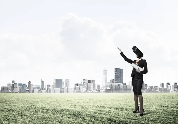 Macchina fotografica diretto donna in piedi su erba verde contro le città moderne — Foto Stock