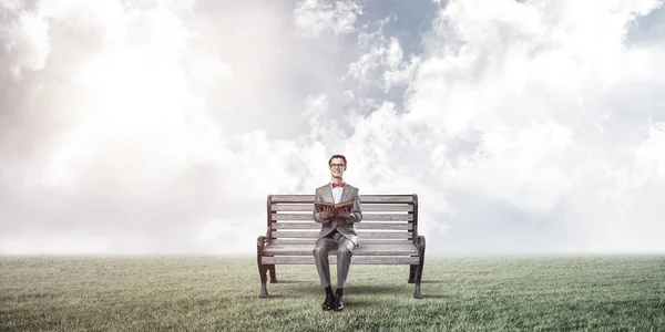 一个戴着红色眼镜 穿着西服 坐在长椅上看书的有趣男人 — 图库照片
