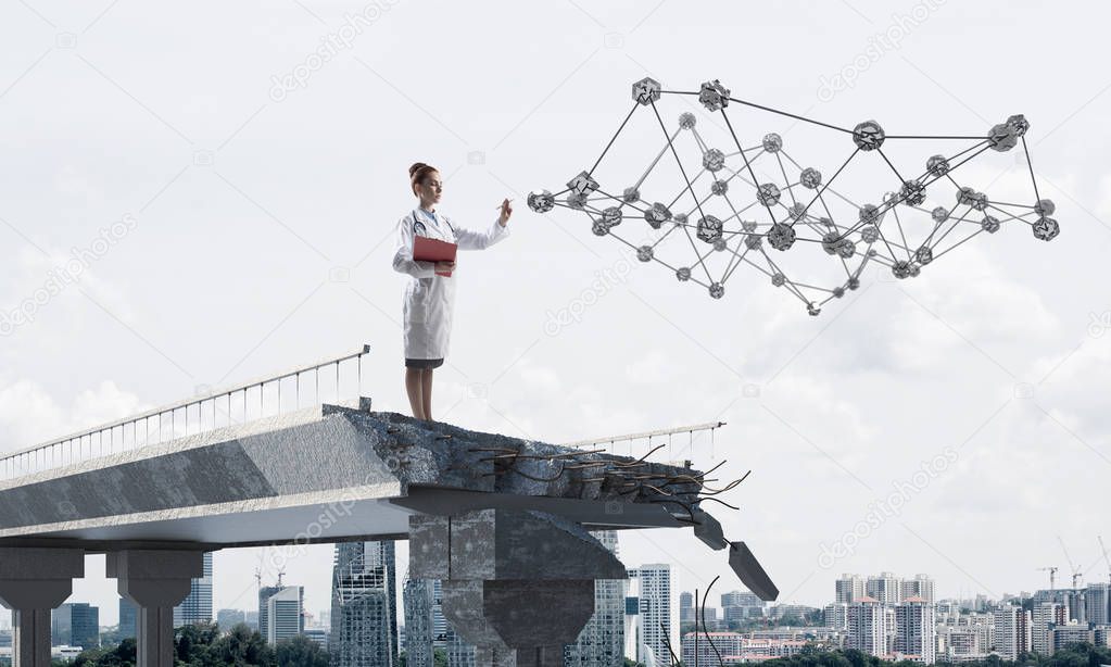 Professional female doctor in white sterile uniform holding notebook in hands while standing on broken bridge. Social network structure and cityscape view on background
