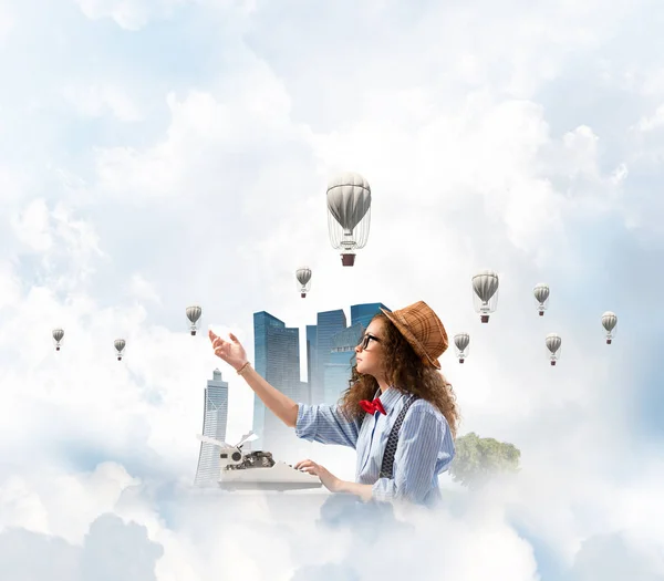 年轻而美丽的女作家在帽子和眼镜使用打字机 而坐在桌子上与浮动城市岛屿和多云的天空景与飞行的空气定子背景 — 图库照片