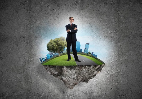 Yeşil yüzen adada beton zemine karşı duran kendine güvenen zarif iş adamı.