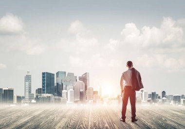 İşadamı arkası dönük duruyor ve şehir manzarasına bakıyor.