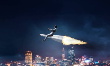 Arka plan üzerinde gece cityscape ve mavi gökyüzü ile roket üzerinde uçan takım elbiseli genç işadamı kavramsal görüntü.
