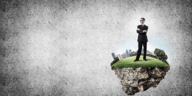 Yeşil yüzen adada beton zemine karşı duran kendine güvenen zarif iş adamı.