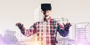 Sanal gerçeklik kulaklığı olan genç bir adam ya da şehrin arka planında 3 boyutlu gözlüklü.