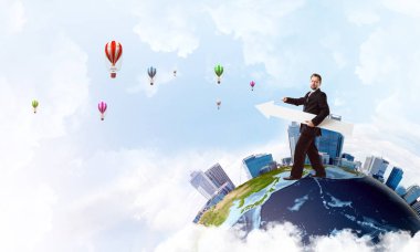 Takım elbiseli başarılı genç iş adamı, Dünya 'da durup uçan balonlar üzerinde dururken ok şeklinde büyük beyaz bir pankartın kenarına işaret ediyor. Bu görüntünün elementleri Nasa tarafından döşenmiştir