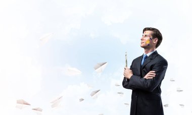Boya fırçası elinde tutan ve uzak duran kağıt uçaklar arka plan üzerinde uçan ile mavi bulutlu gökyüzü karşı arayan genç düşünceli adam portresi.