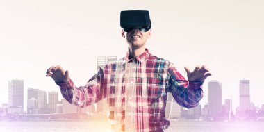 Sanal gerçeklik kulaklığı olan genç bir adam ya da şehrin arka planında 3 boyutlu gözlüklü.