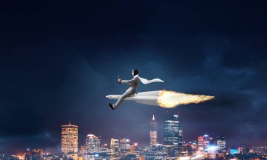 Arka plan üzerinde gece cityscape ve mavi gökyüzü ile roket üzerinde uçan takım elbiseli genç işadamı kavramsal görüntü.