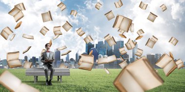 Kırmızı gözlüklü ve takım elbiseli komik adam bankta oturup kitap okuyor.