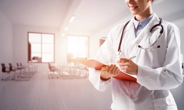 明るい病院の建物の中に立っている間ノートにノートを作る白い医療制服に自信を持って女性医師のクローズ アップ 医療業界の概念 — ストック写真
