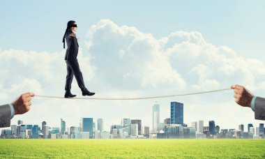 Gözlerinde perde olan bir iş adamı şehrin arka planında ipte yürüyor.