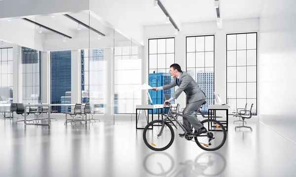 Businessman with paper documents in hand on bike. Accountant in business suit riding bicycle at conference room. Paperwork express service. Corporate office life concept with modern business workspace