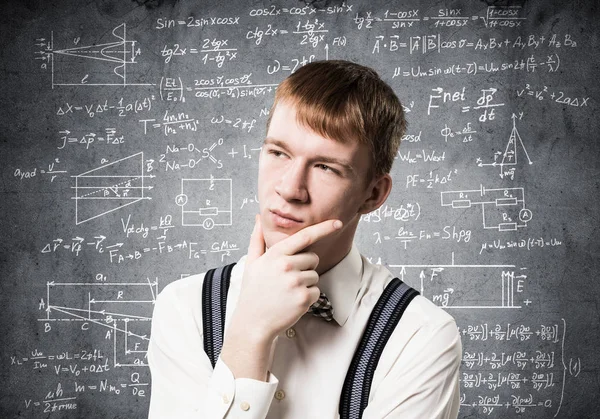 赤毛の生徒は上を向いて何かを思い出そうとします パズル少年は数学計算をしている 男はシャツを着て 数学式と黒板の背景にサスペンダー — ストック写真