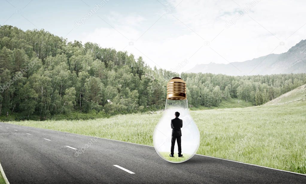 Young businessman trapped inside of light bulb on asphalt road