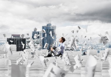 Düşünceli işadamı, arka planda şehir manzarası olan uçan gazeteler arasında bir yığın belgeyi incelerken başka tarafa bakıyor. Karışık ortam.