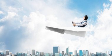 Kağıt uçakta oturan pilot ile iş liderliği ve motivasyon konsepti. Havacı şapkalı komik adam ve şehrin üzerinde kağıt uçak süren gözlükler. Yüksek binalarile modern megapolis.